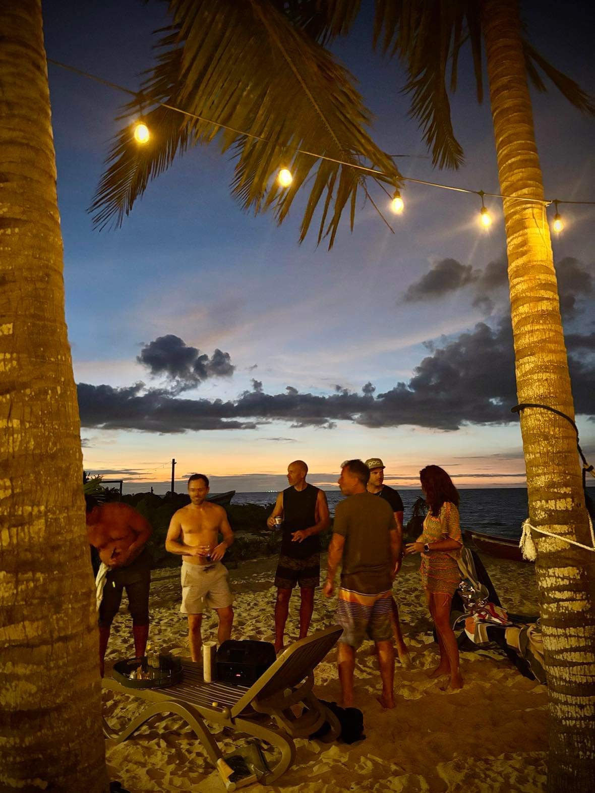 Friends gathered on the beach under string lights at sunset