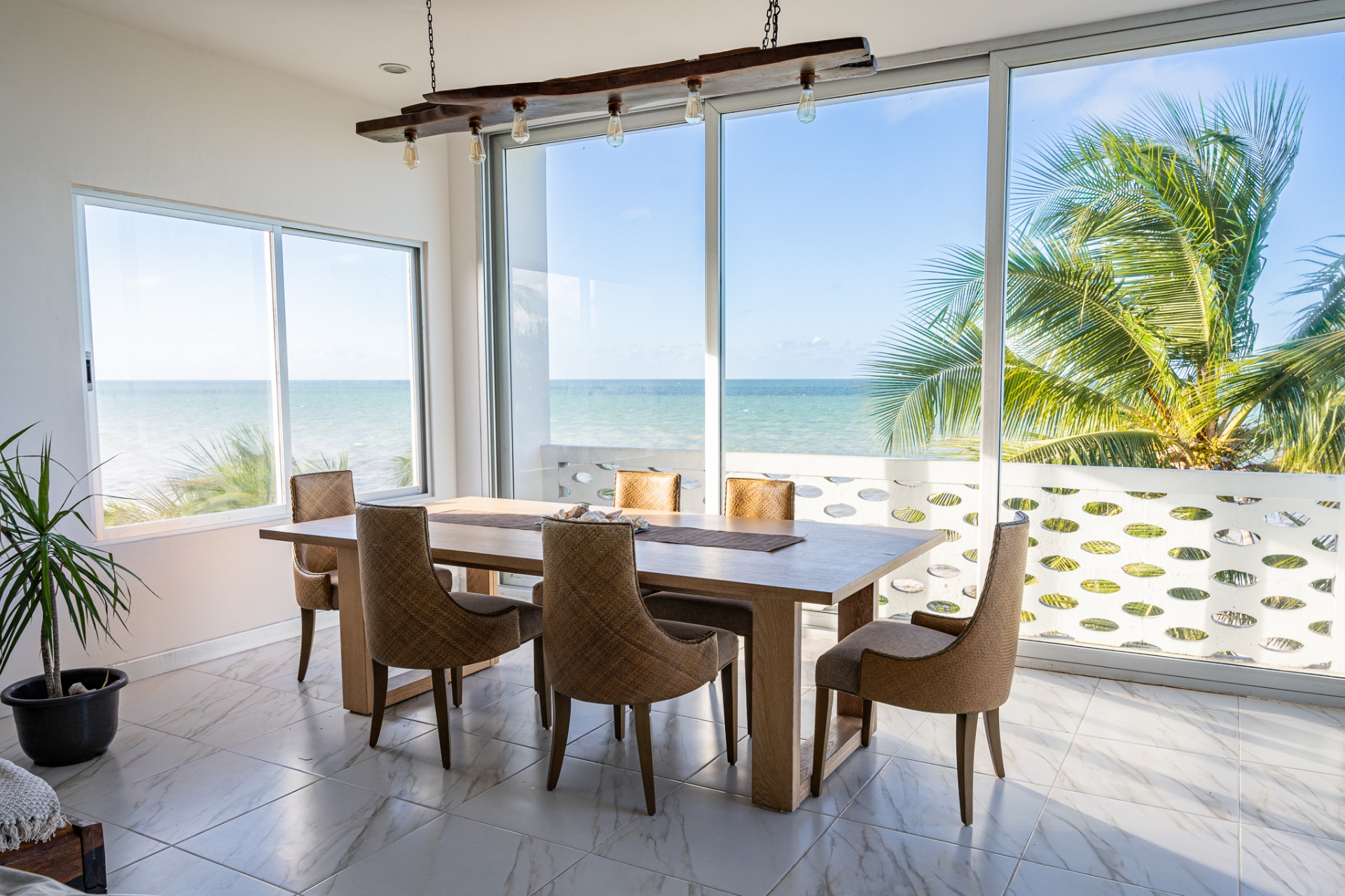 Dining table beside floor-to-ceiling windows facing the turquoise sea