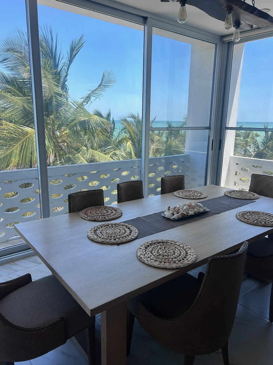 Dining table set with placemats and ocean view through palms